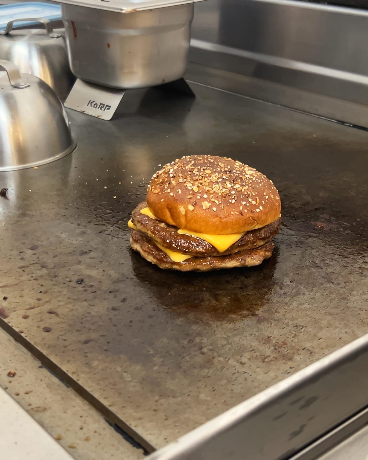 Enztal Burger mit doppeltem Patty und geschmolzenem Cheddar auf der heißen Grillplatte, die Glocke gerade abgehoben