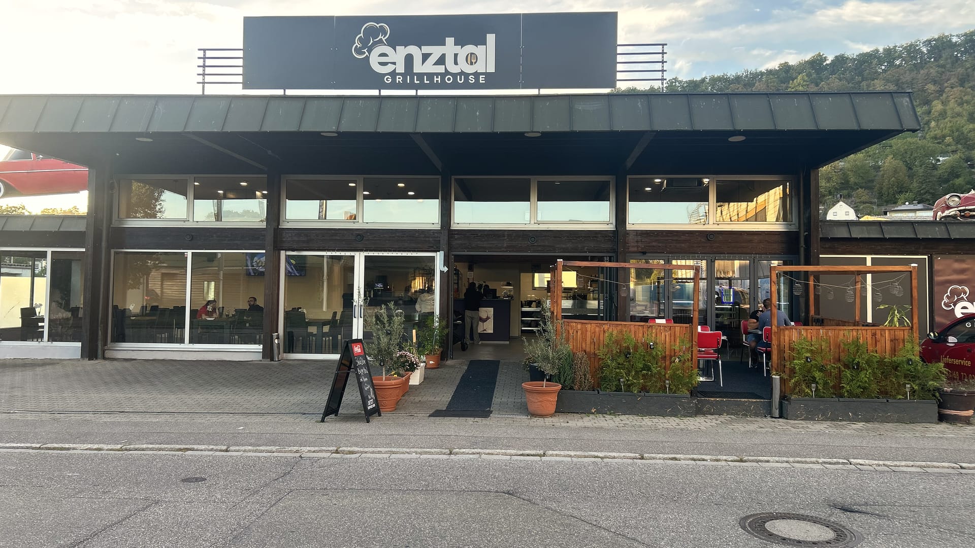 Enztal Grillhouse bei Tag: Fassade mit Schild und Terrasse, Parkplätze davor