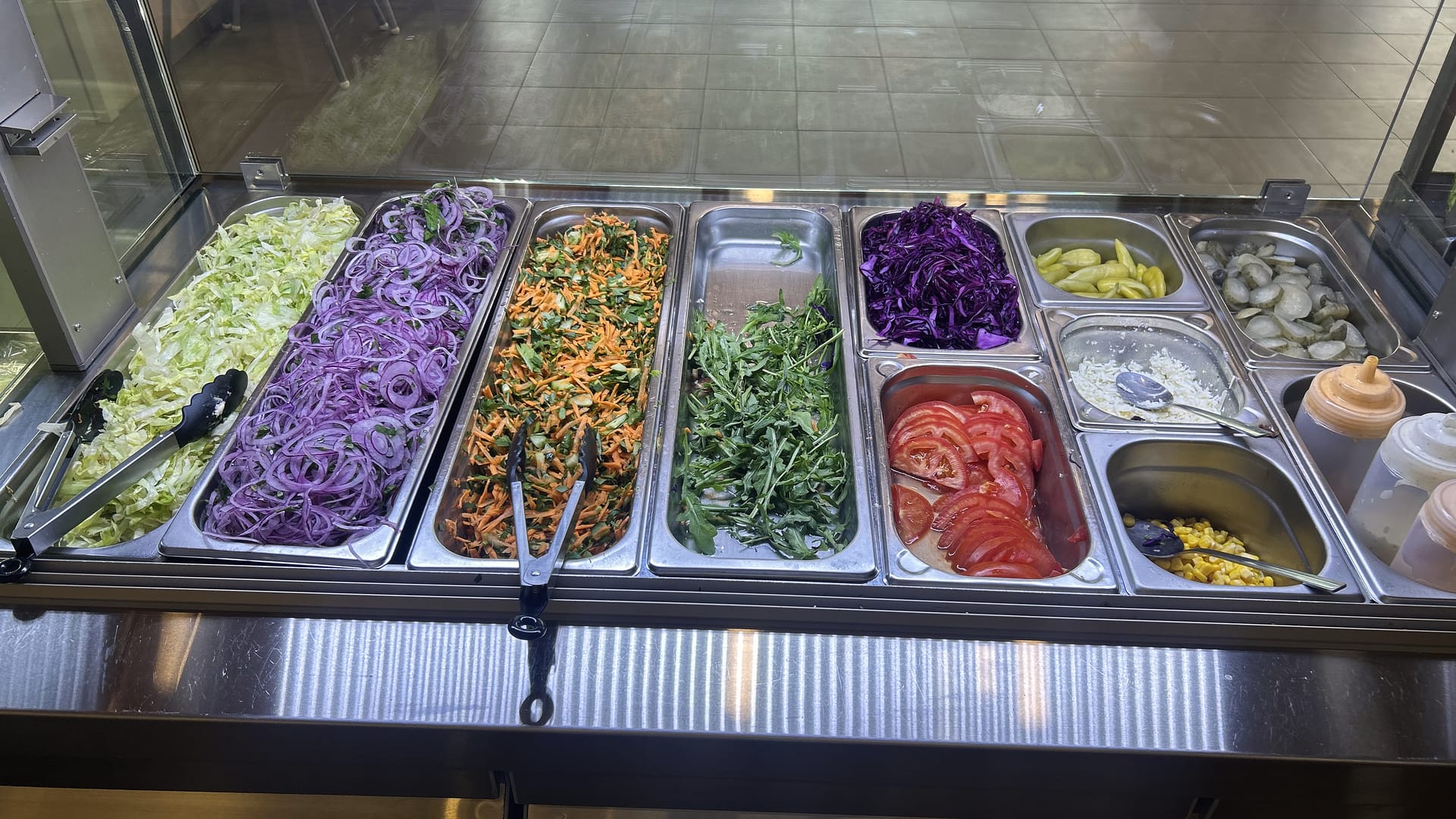 Die Salatbar: Rotkohl, Zwiebeln, Rucola, Tomaten und Peperoni in Edelstahlschalen